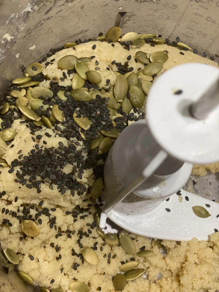 Cookie dough mixture with black sesame seeds and pumpkin seeds in a food processor.