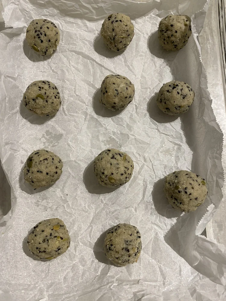 Cookie dough balls with black sesame seeds and pumpkin seeds on parchment paper, ready for baking.