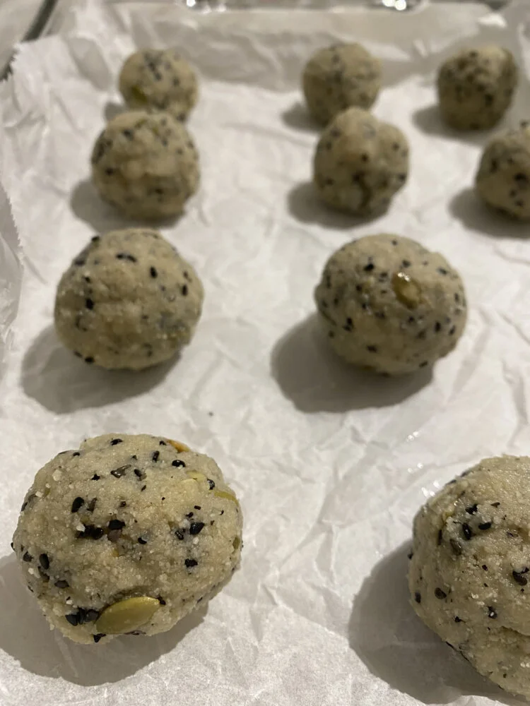 Cookie dough balls with black sesame seeds and pumpkin seeds on parchment paper, ready for baking.