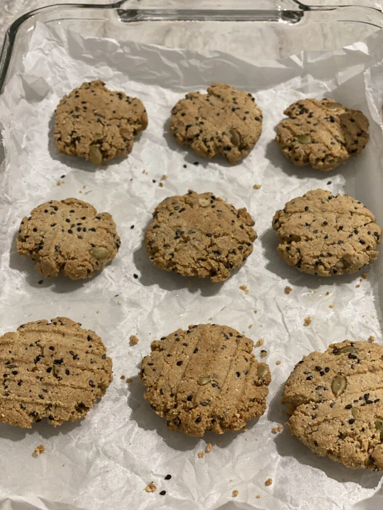 Baked almond cookies with black sesame seeds and pumpkin seeds on parchment paper in a glass baking dish.