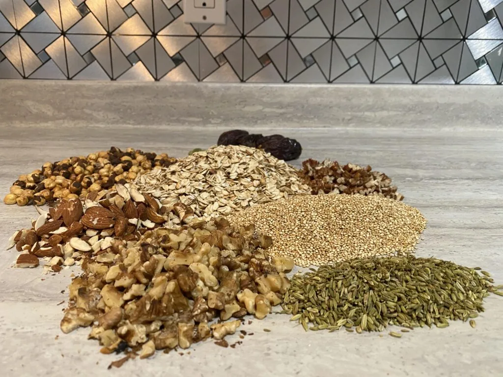 Ingredients for protein bars, including oats, nuts, quinoa, and fennel seeds, arranged on a countertop.