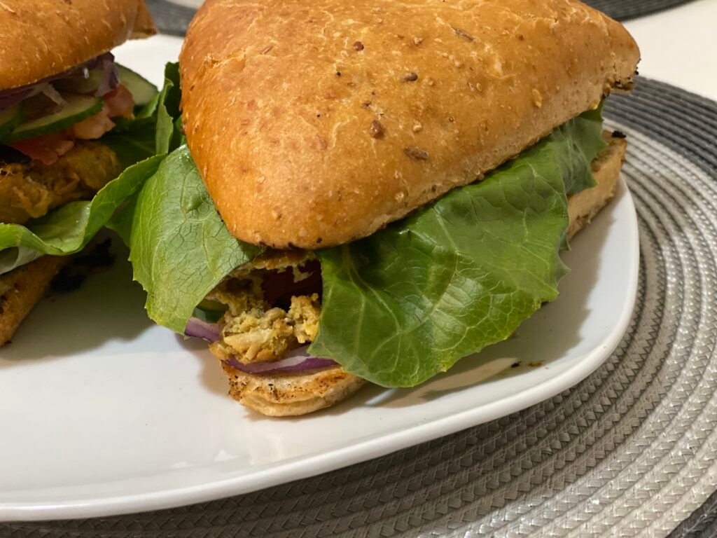 A close-up of a gluten-free burger with a triangular bun, fresh lettuce, red onion, and flavorful fillings, served on a white plate.