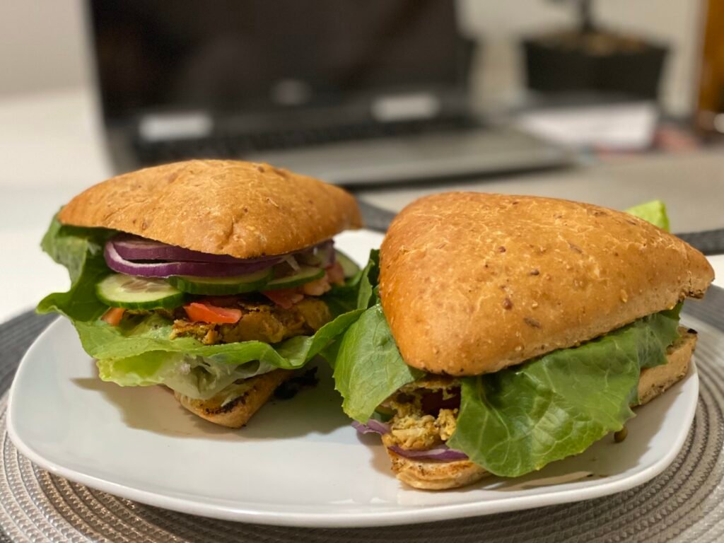 Two gluten-free burgers with triangular buns, fresh lettuce, cucumbers, tomatoes, and red onions, served on a white plate.