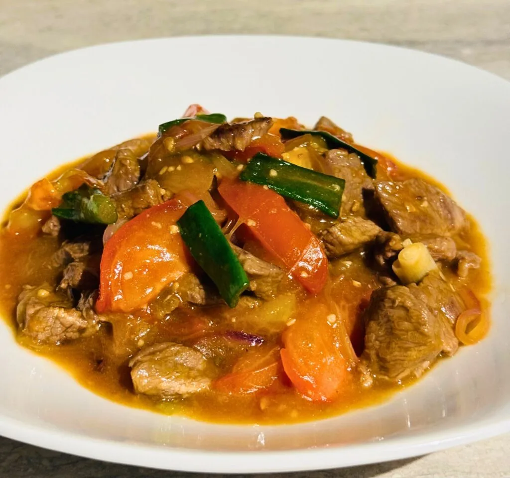A bowl of beef tomato stir-fry with tender beef, tomatoes, and green onions in a rich sauce.