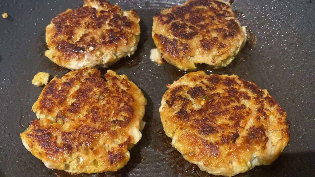 Golden-brown fish cutlets sizzling in a pan.