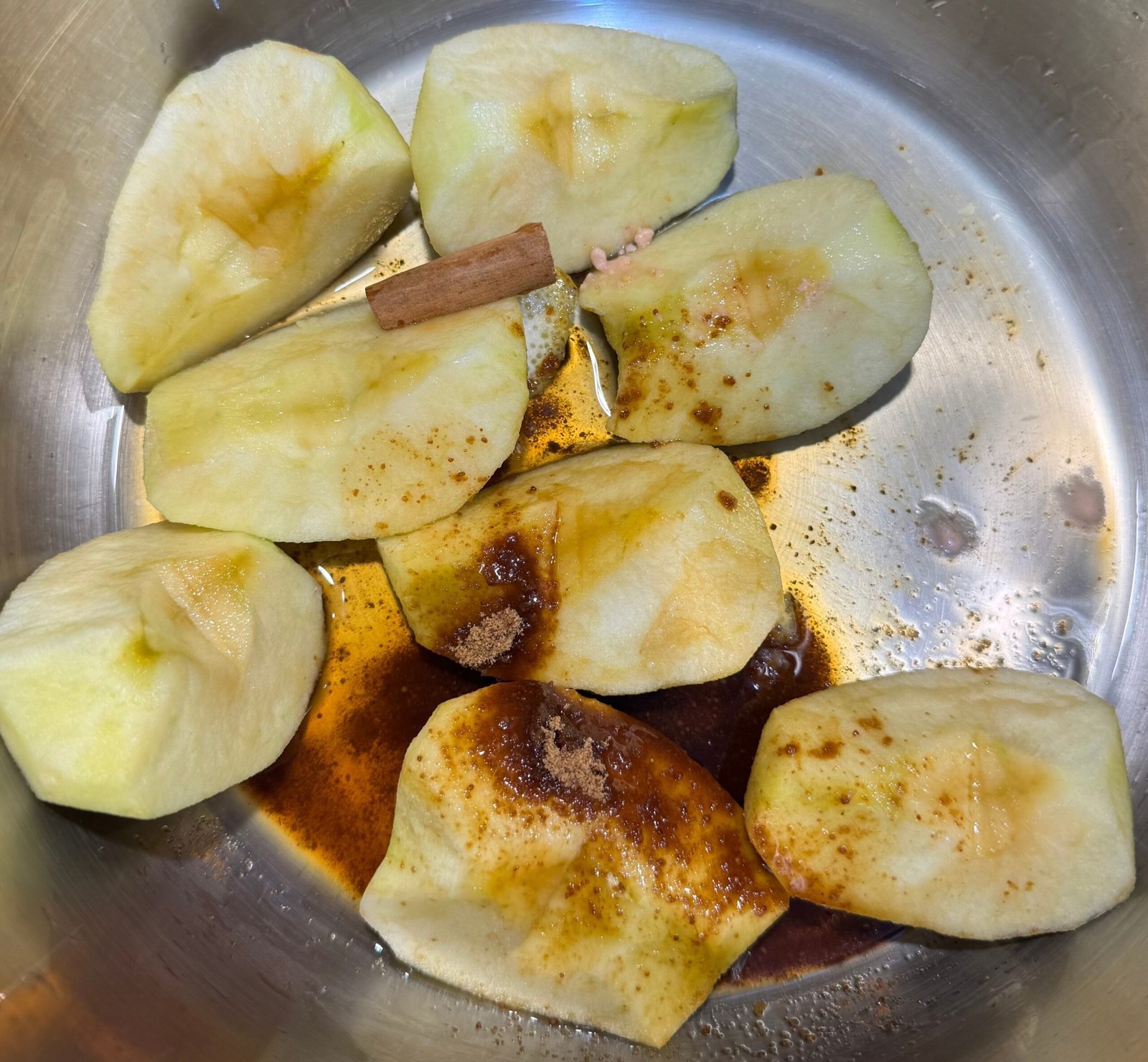 Close up of peeled apple quarters with Ceylon cinnamon stick, coconut sugar, and spices in a stainless steel pot before simmering