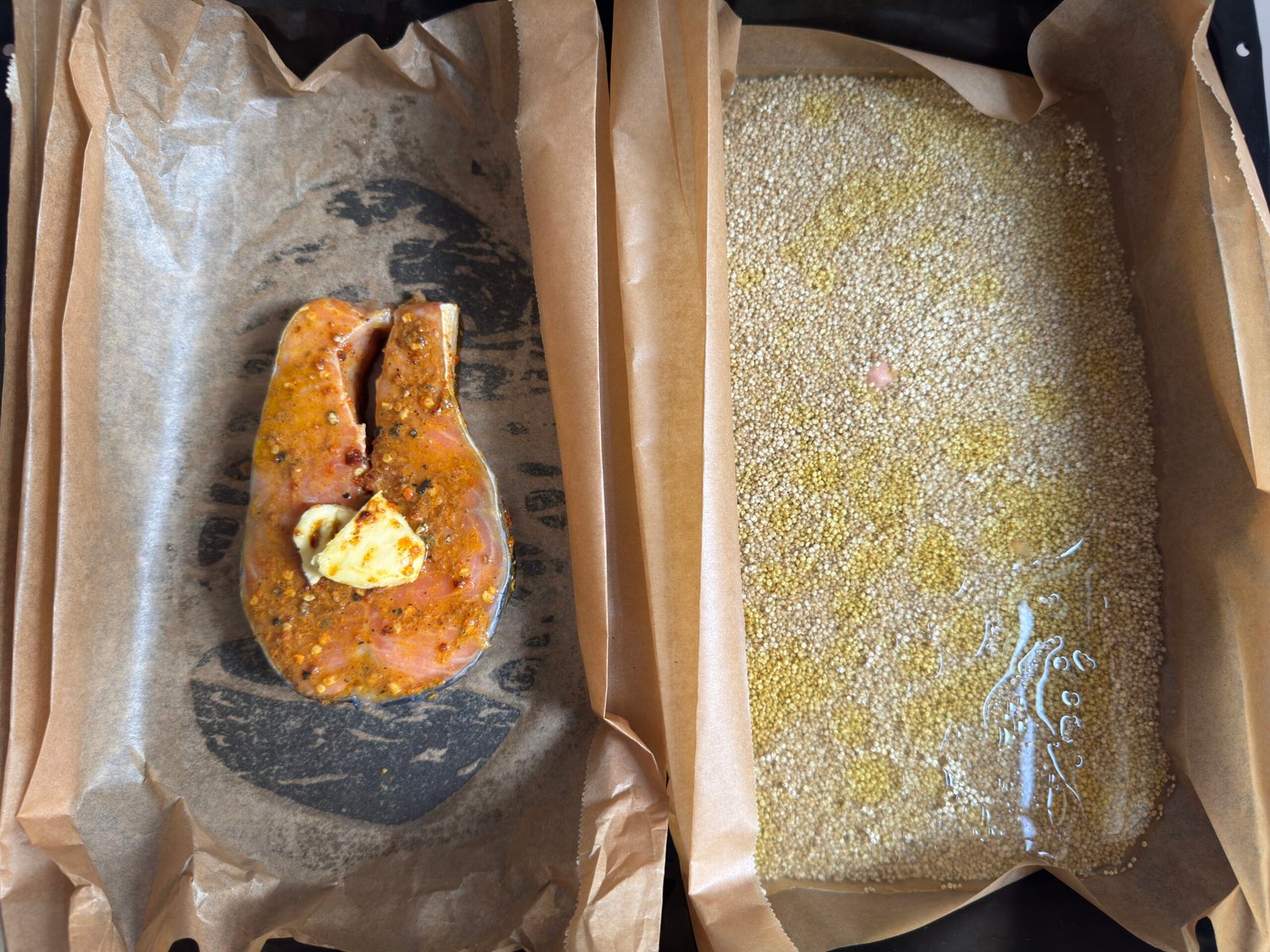 Baking tray divided with parchment paper showing marinated salmon steak on the left and quinoa on the right, ready for baking.
