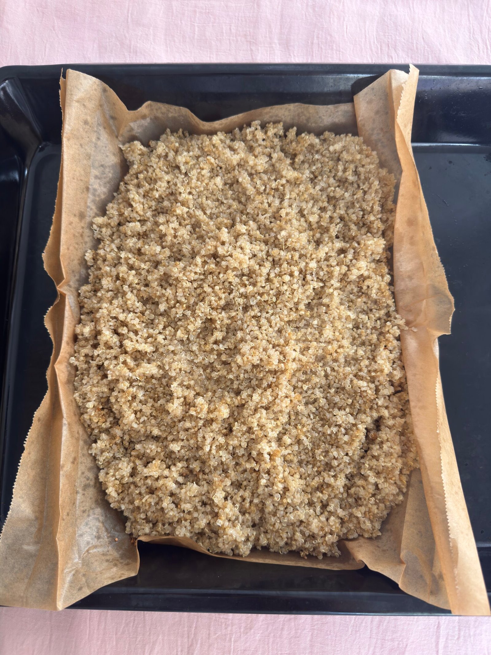 Cooked fluffy quinoa spread on parchment paper in a baking tray after baking is complete.