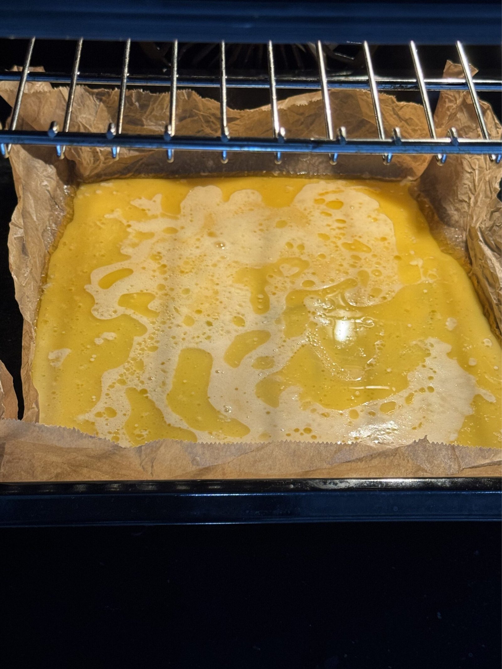 Gluten-free Dutch baby batter in a parchment-lined baking tray inside the oven ready to bake
