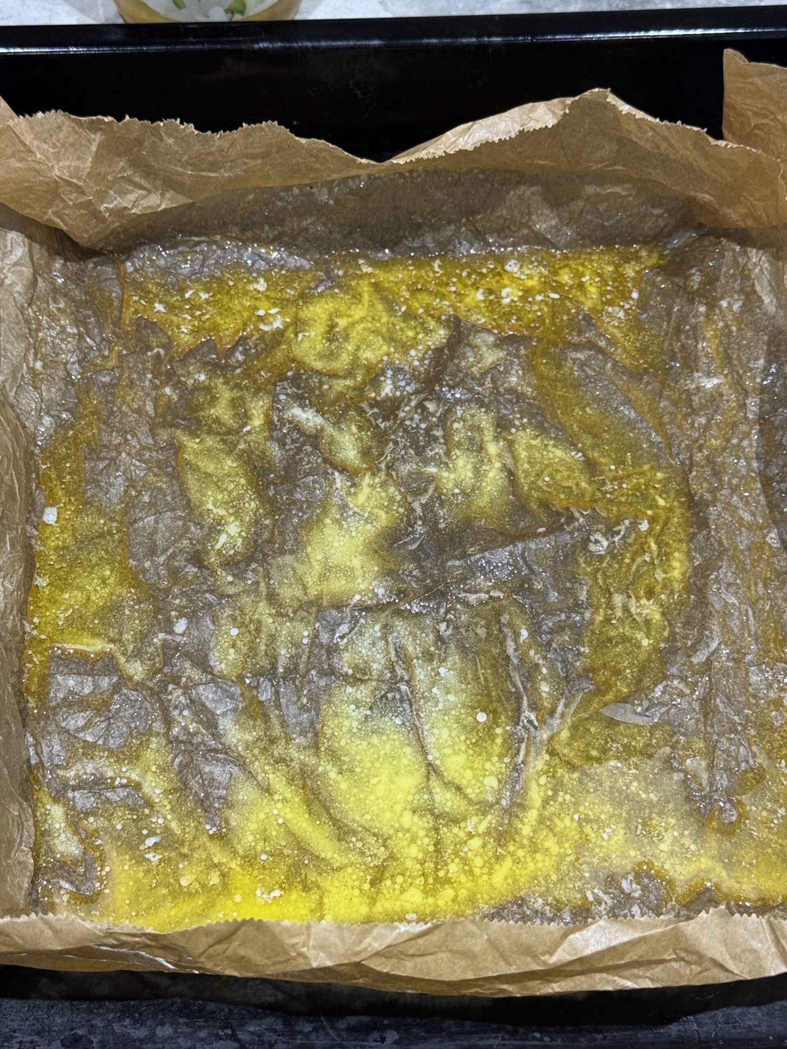 Hot melted butter bubbling and coating baking paper in a lined baking tray, ready for Dutch baby batter