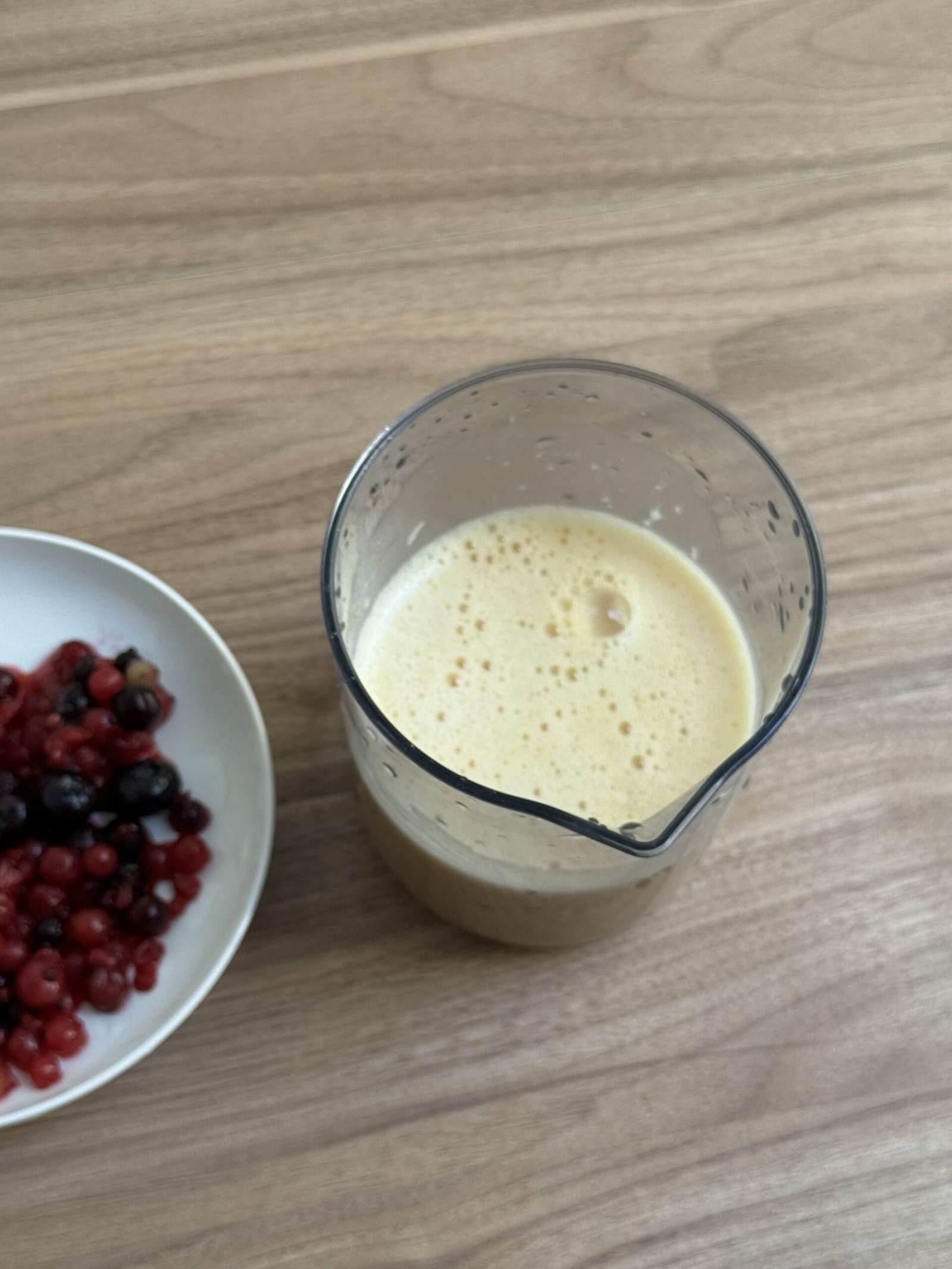Smooth frothy Dutch baby batter in a blender jug next to a bowl of mixed red and black berries
