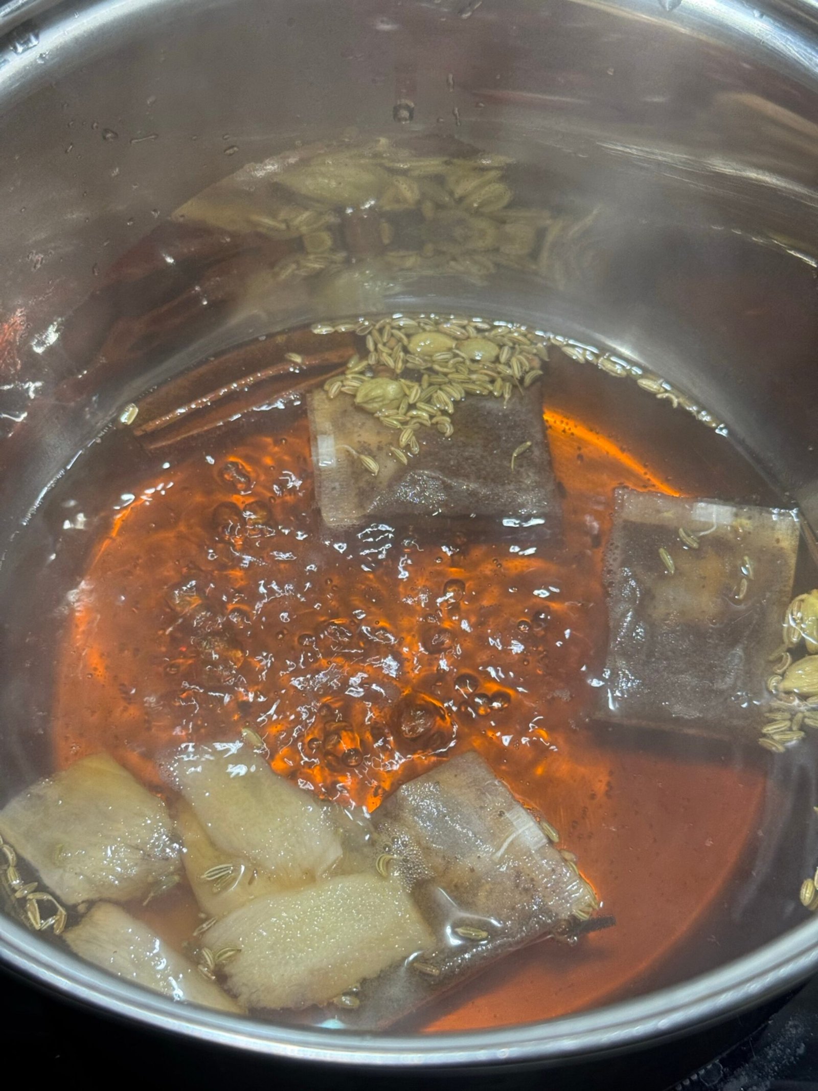 Tea bags and whole spices simmering in water that has turned a deep reddish-burgundy color.