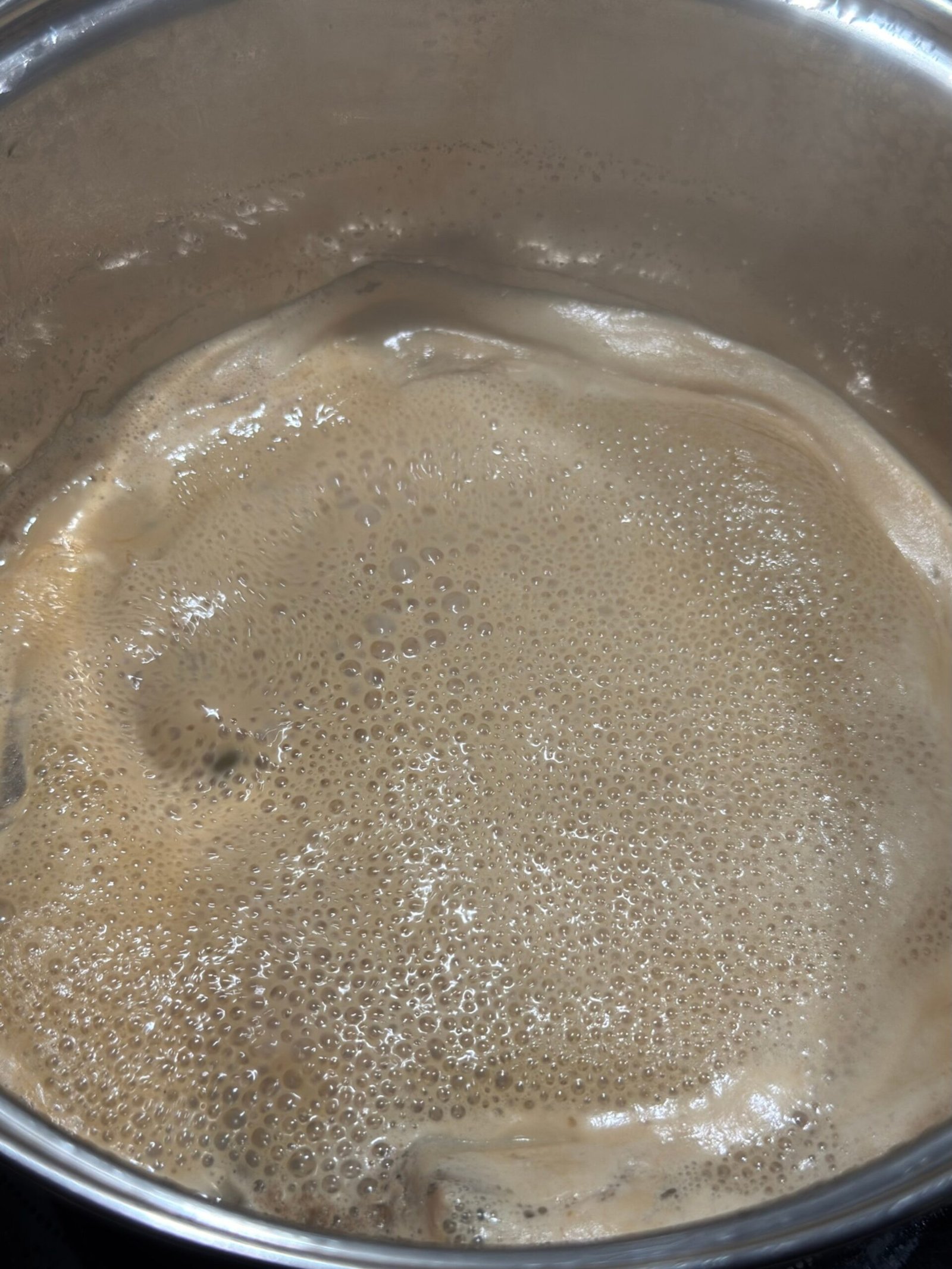 Masala chai at a rolling boil in a saucepan, frothy and light brown after the milk has cooked down.