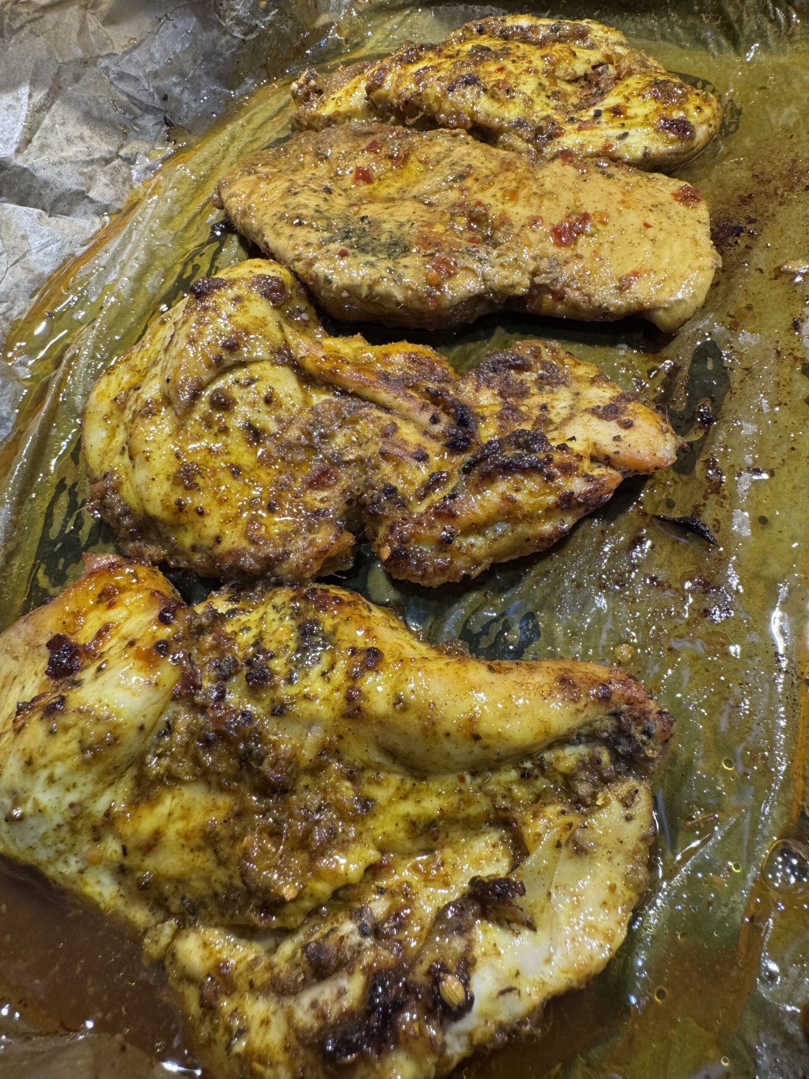 Freshly baked chicken breasts resting in their cooking juices on parchment paper, showing a rich, golden-brown crust from the roasted spices.