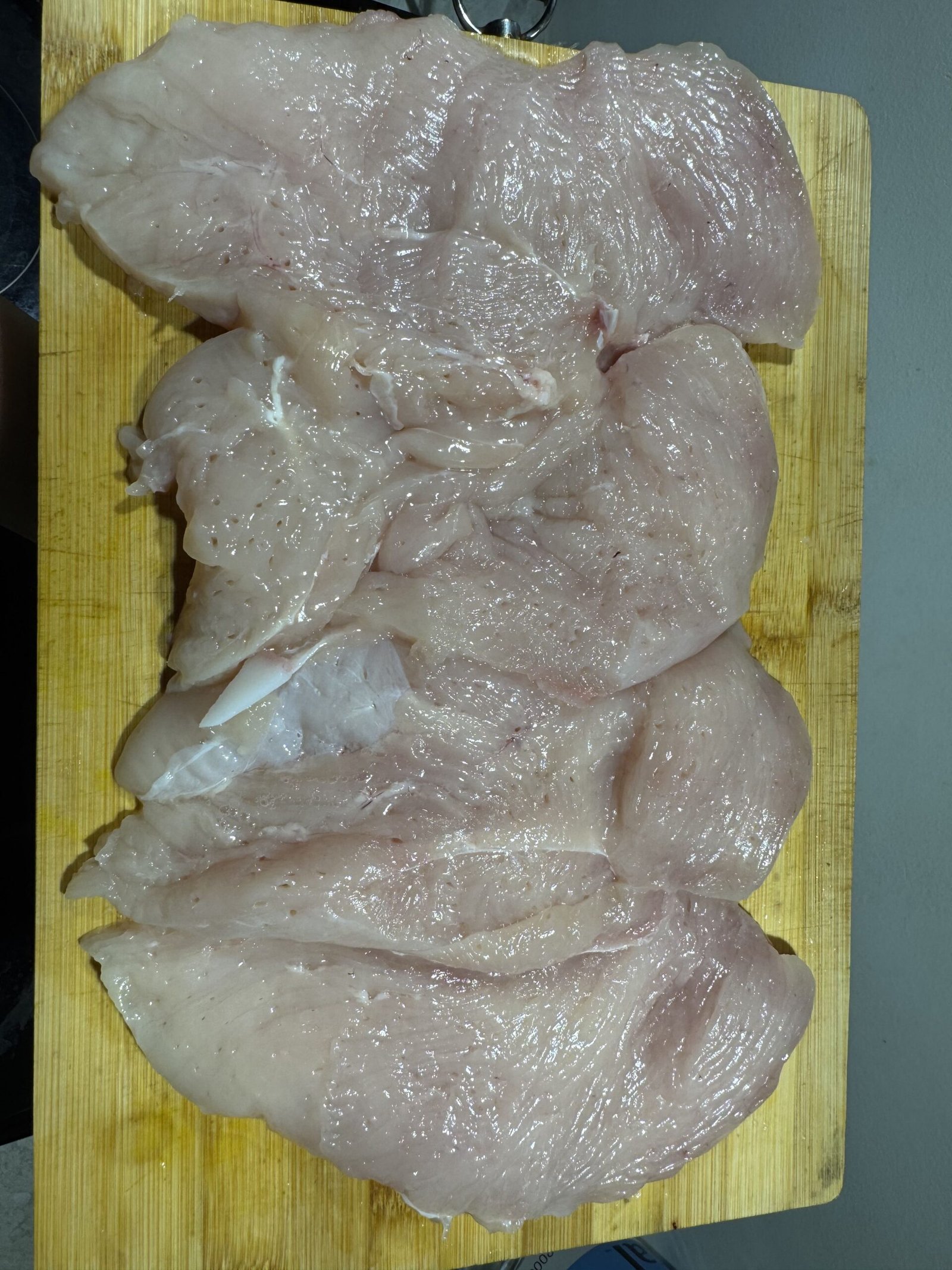 Four raw, unseasoned chicken breasts resting flat on a wooden cutting board.