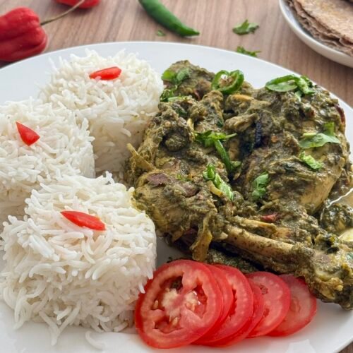 Palak chicken served on a white plate with steamed basmati rice, sliced tomatoes, fresh green chilies, and roti on the side.