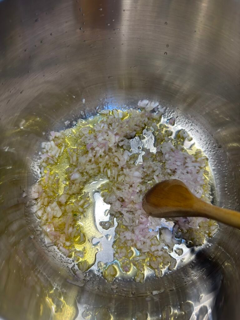 Finely chopped onions frying in oil in a heavy-bottomed pan with a wooden spoon.