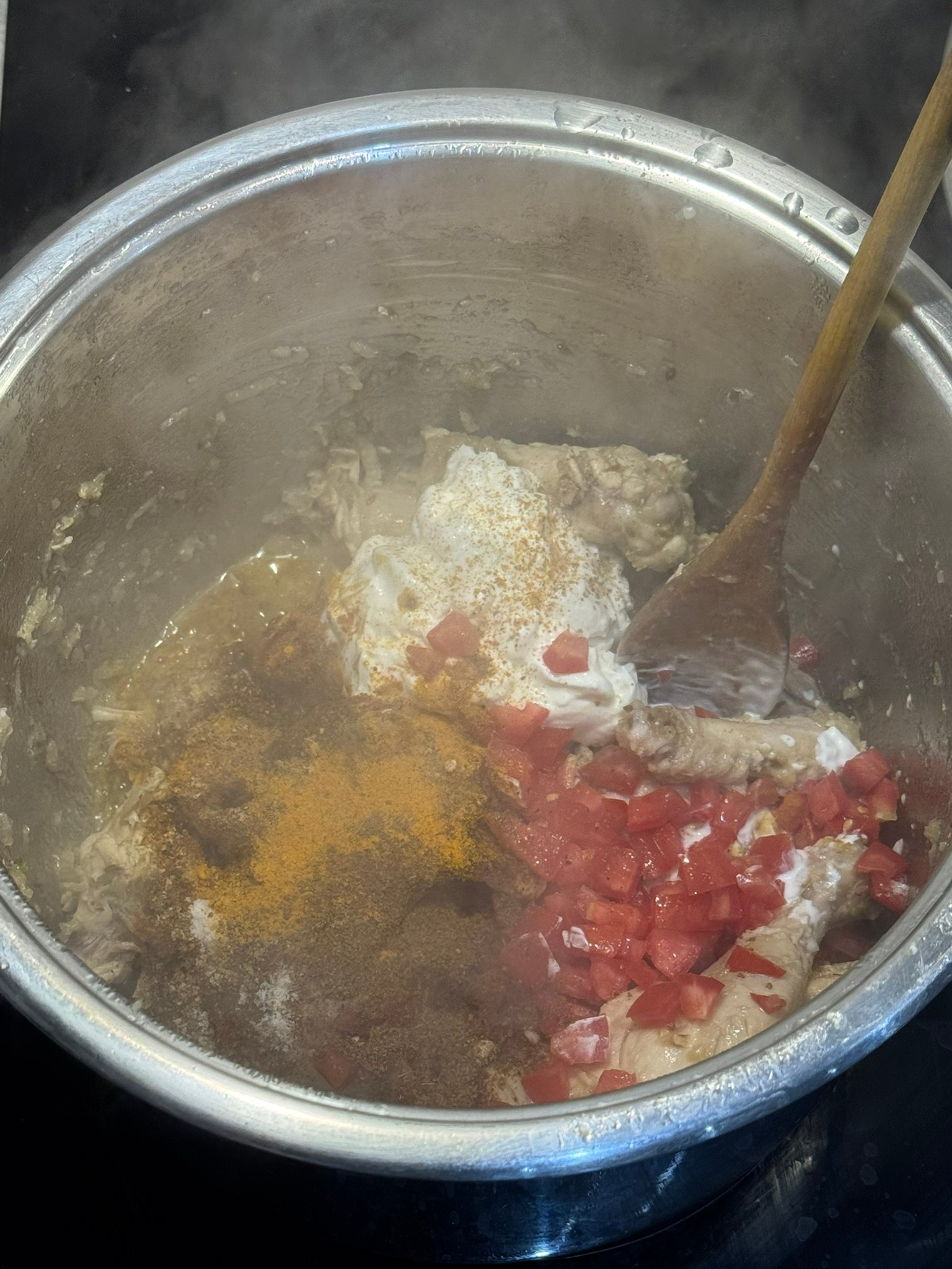 Chopped tomatoes, yogurt, and ground spices (turmeric, coriander, cumin) added to the chicken in the pan for the bhunai step.