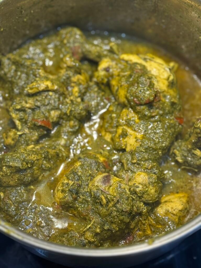 Palak chicken simmering in the pot with the spinach fully mixed into the curry, oil starting to separate around the edges.
