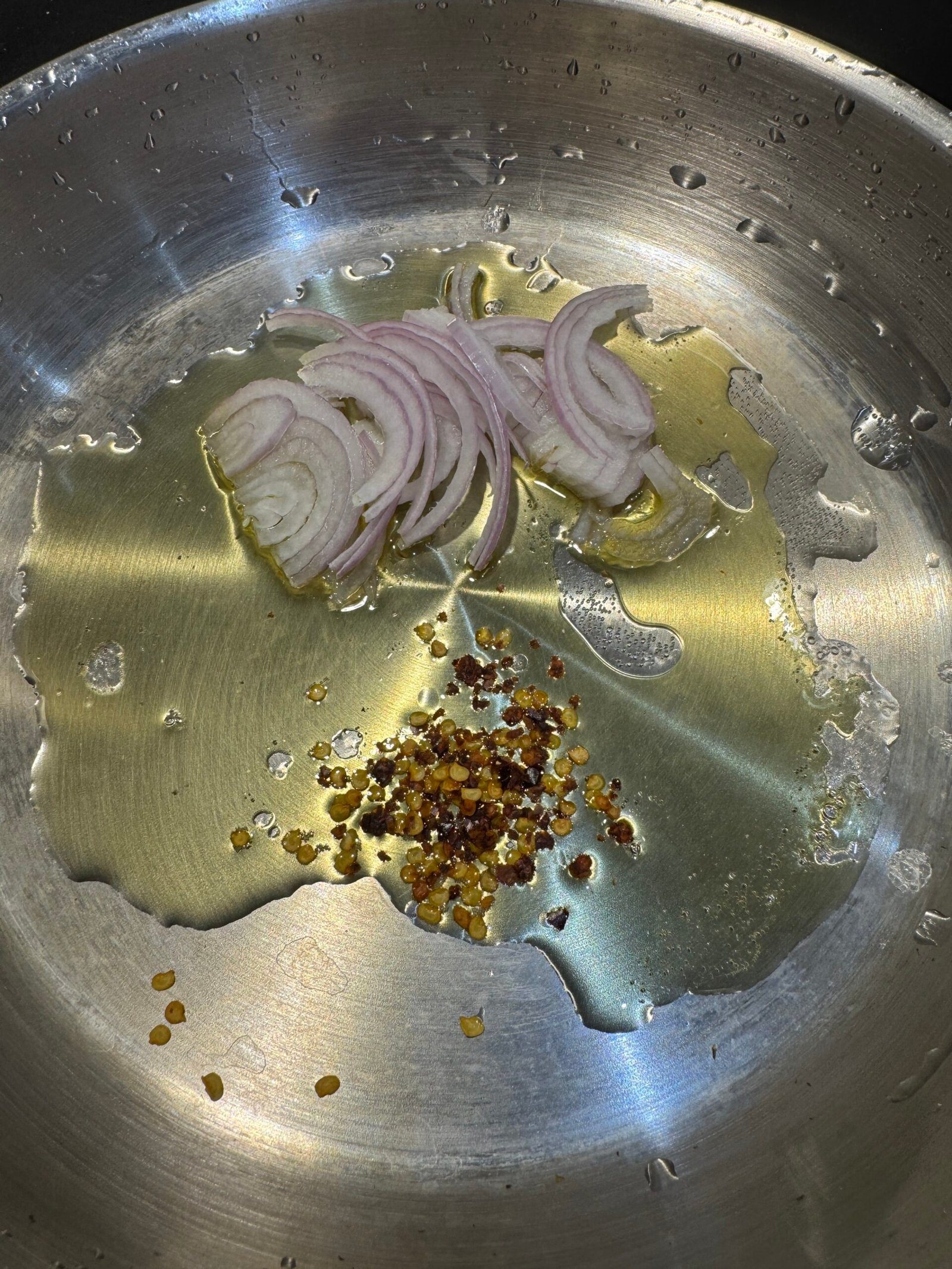 Sliced onion and red chili flakes frying in desi ghee in a small pan for the ghee tarka finish.