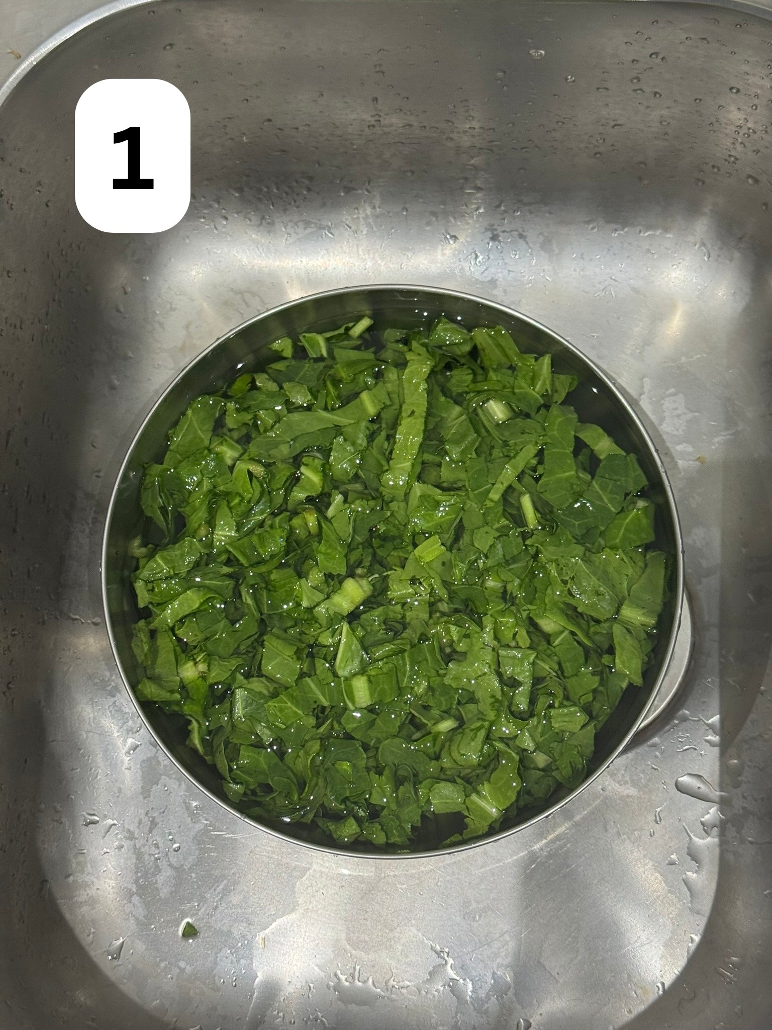 Washed and chopped fresh spinach in a steel bowl, ready for blanching.