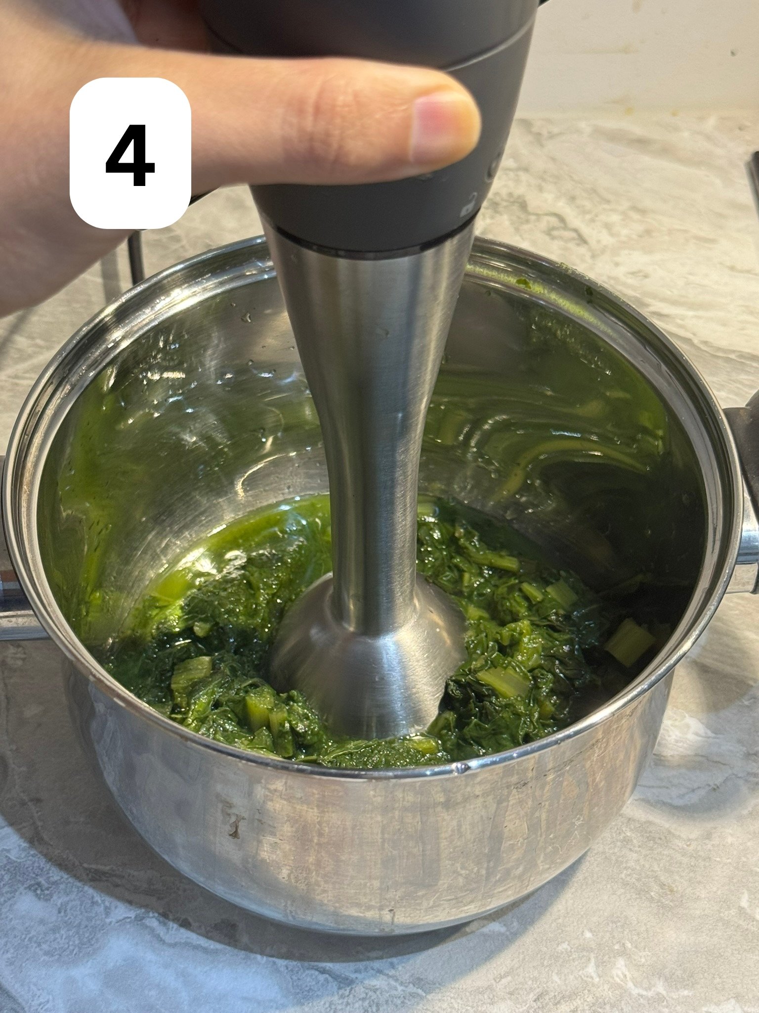 Blanched spinach being blended into a smooth paste using a hand blender (immersion blender).