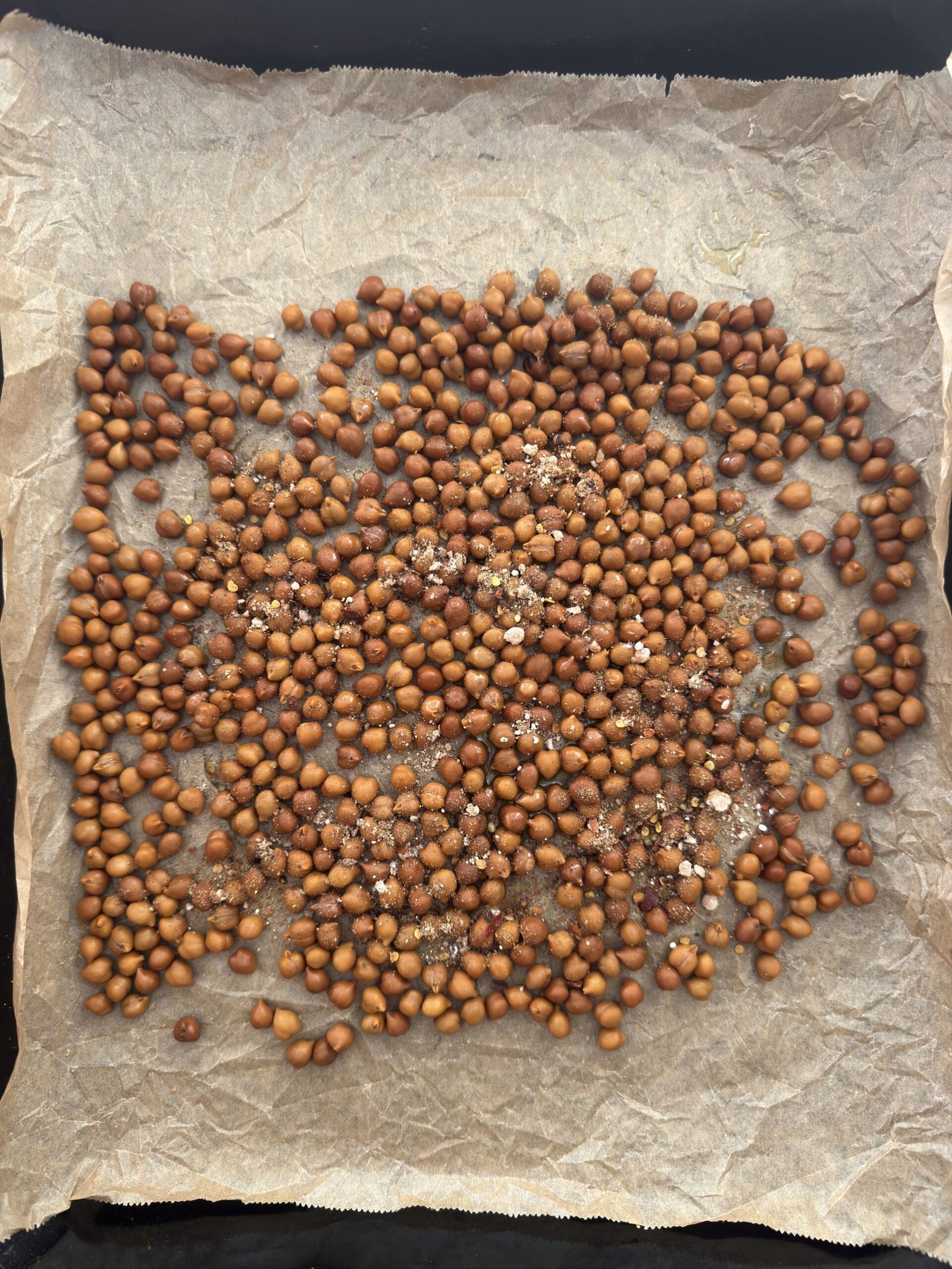 Chickpeas spread on parchment paper on a baking tray, tossed with olive oil and spices, showing the even coating step before roasting.