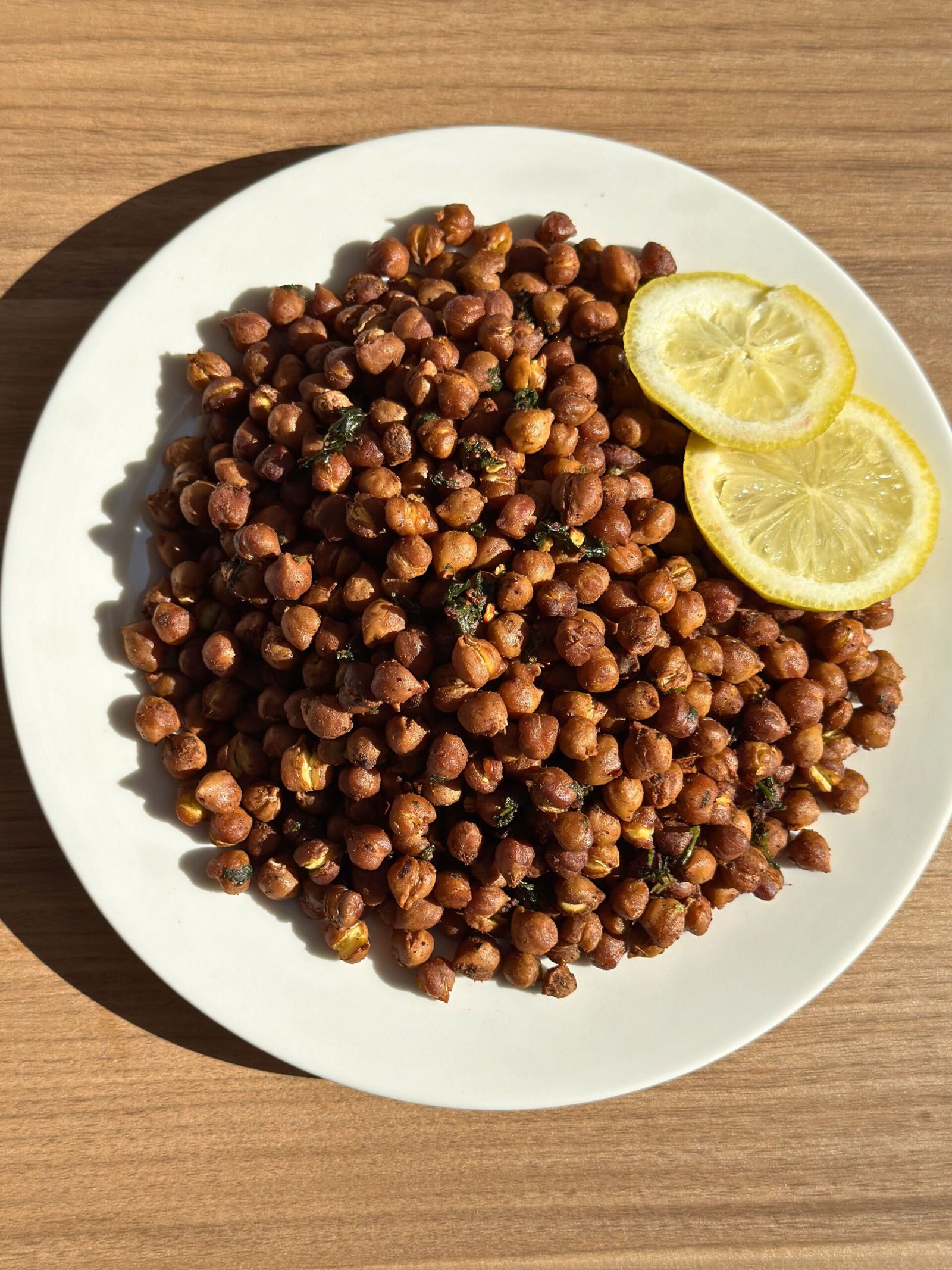 Roasted black chickpeas heaped on a white plate with fresh cilantro scattered over the top and lemon slices as garnish, showing the final plated result.