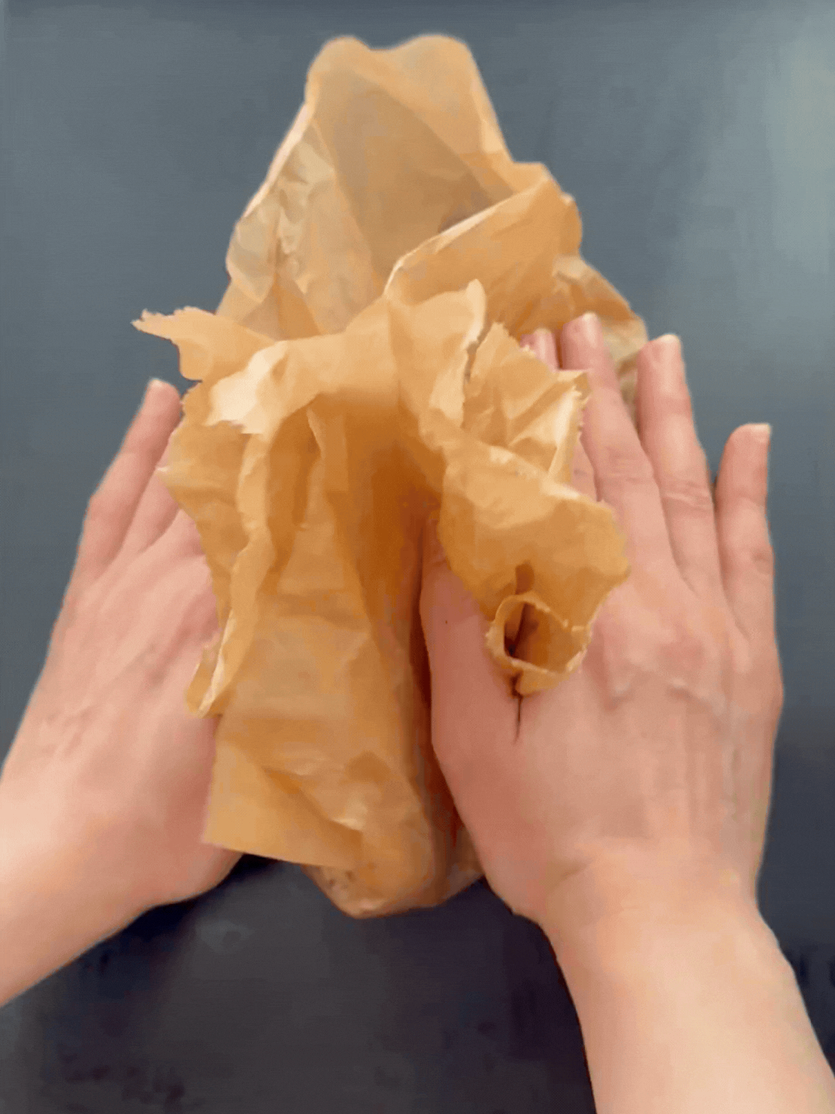 Close-up of hands holding the four corners of parchment paper bunched together, demonstrating the no-mess method of massaging the spices and oil into the chickpeas without getting hands dirty.