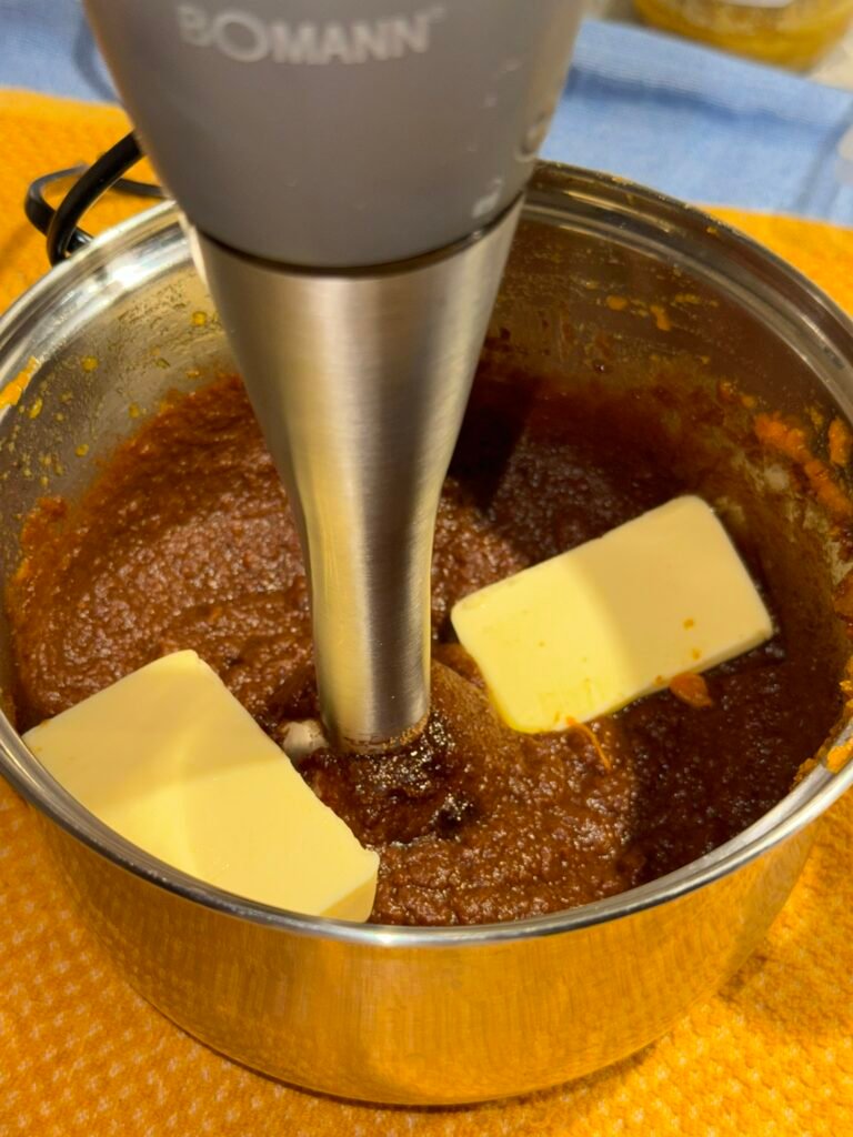 Blocks of dairy-free butter alternative being blended into sweet potato and cocoa mixture with an immersion blender to make chocolate frosting.