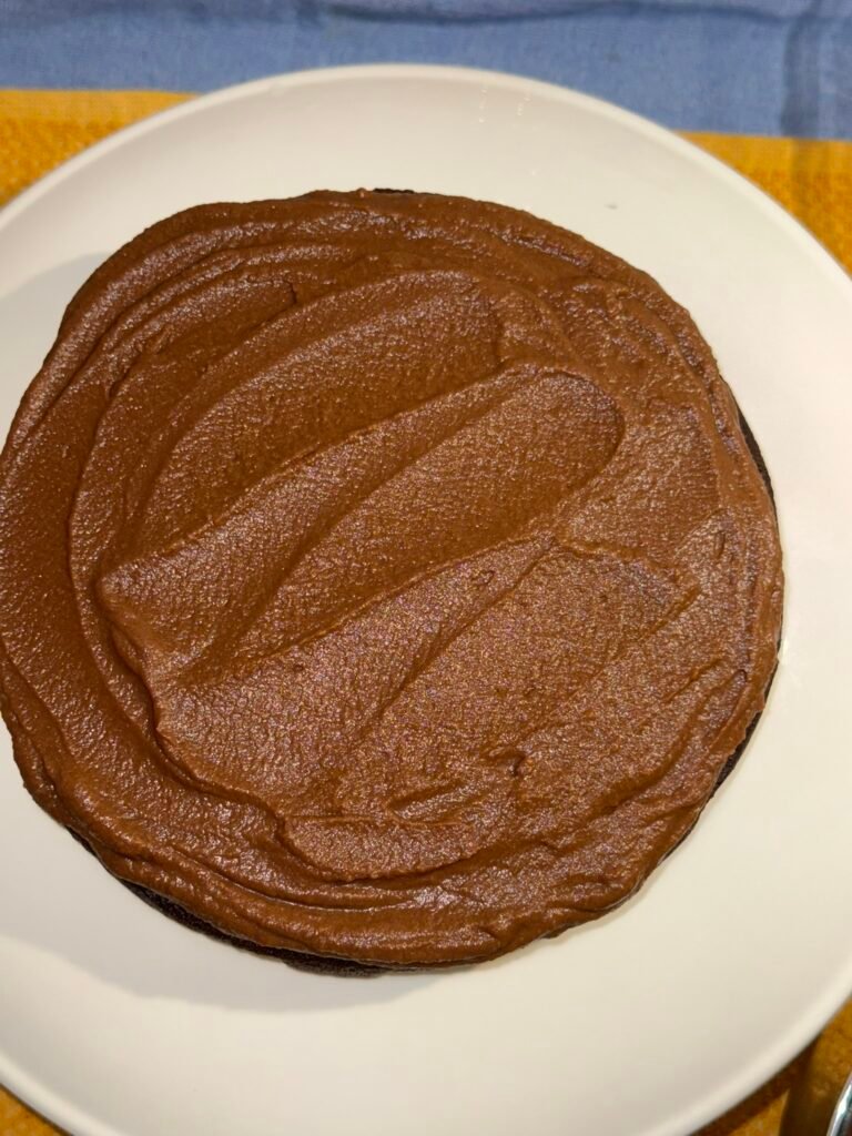 Bottom layer of gluten-free chocolate cake spread with chocolate sweet potato frosting on a white plate.