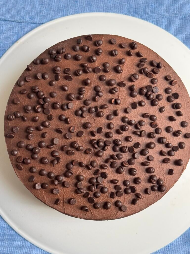 Whole gluten-free chocolate cake frosted with chocolate sweet potato frosting and topped with mini chocolate chips, viewed from above.