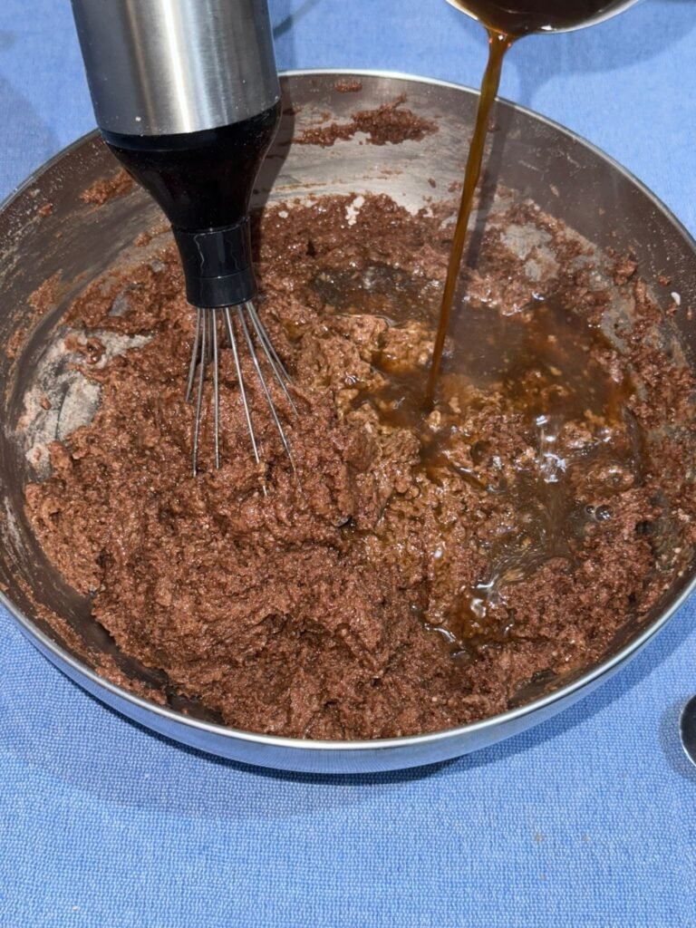 Brewed coffee being poured into gluten-free chocolate cake batter while blending with an immersion blender.