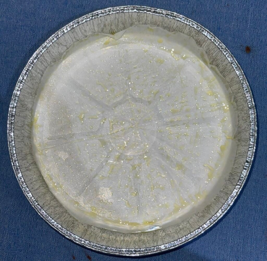 Empty foil cake pan lined with parchment paper and greased with oil, ready for chocolate cake batter.