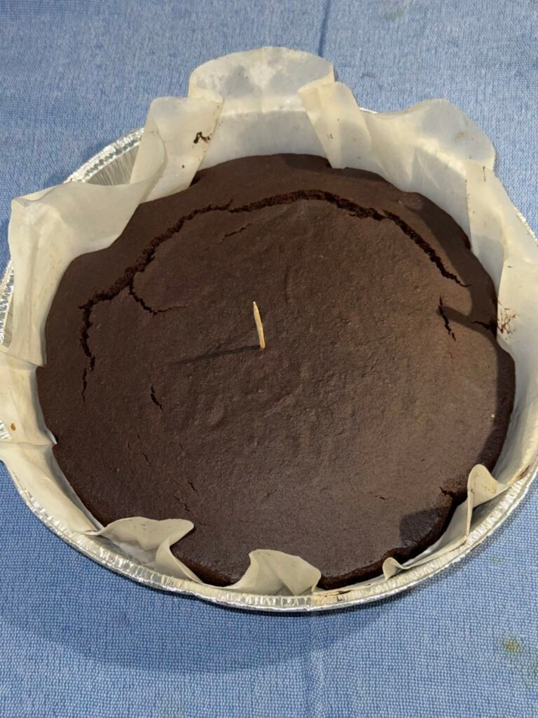 Baked gluten-free chocolate cake in a parchment-lined pan with a toothpick inserted in the center to test doneness