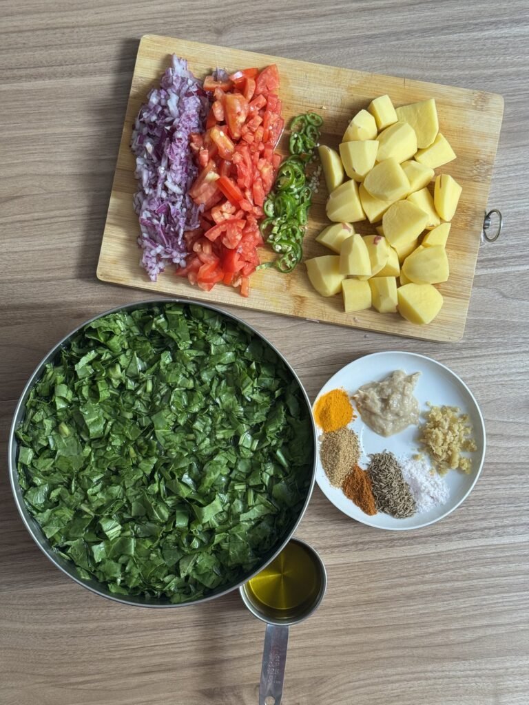 Prepped ingredients for aloo palak including chopped onion, tomato, green chili, cubed potatoes, chopped spinach, and spices