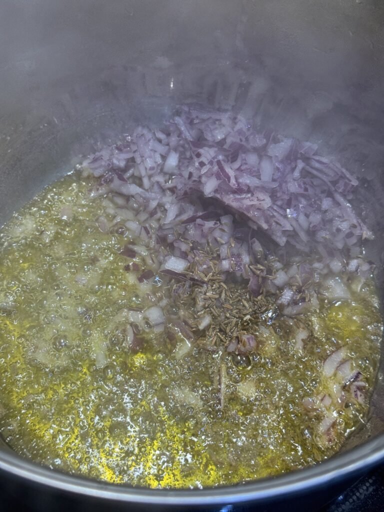 Chopped red onion and cumin seeds frying in oil in a steel pot for aloo palak