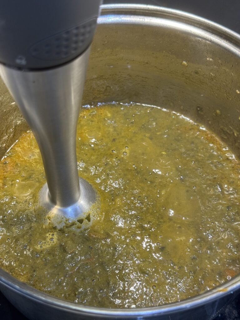 Hand blender pureeing cooked spinach into a smooth green gravy